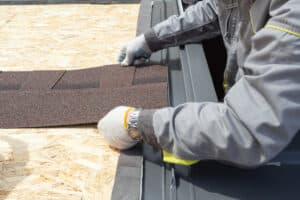 Professional roofer laying asphalt shingles sheet on the roof