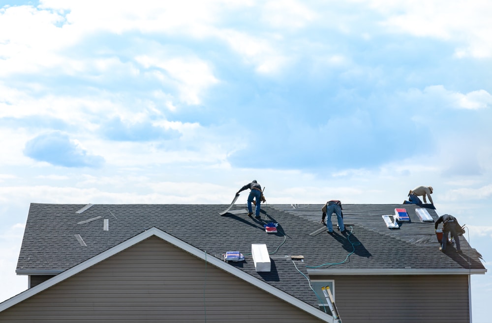 Four construction workers lay shingles on top of a house