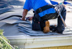 A worker replaces shingles on the roof of a house