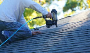 Handyman using nail gun to install shingle to repair roof