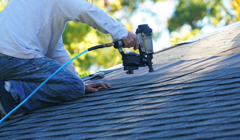 Handyman using nail gun to install shingle to repair roof