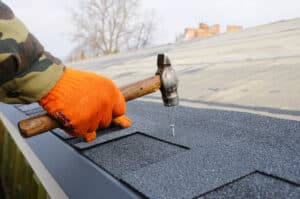 Worker hands installing bitumen roof shingles using hammer in nails