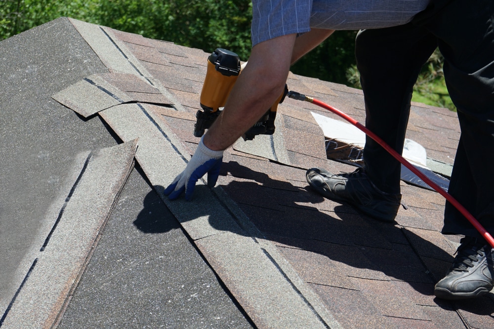 A roofer nailing asphalt shingles with an air gun