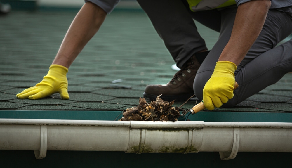 A male worker clears a clogged roof gutter from dirt, debris and fallen leaves