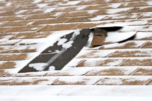 Damaged roof shingles blown off a home from a windy winter storm with strong winds