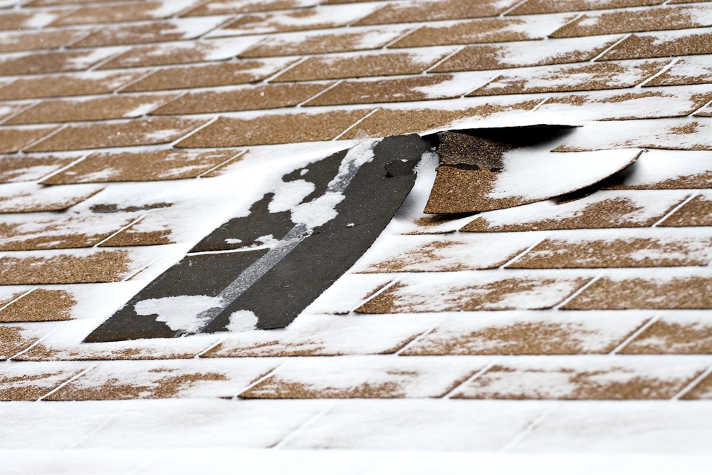 Damaged roof shingles blown off a home from a windy winter storm with strong winds