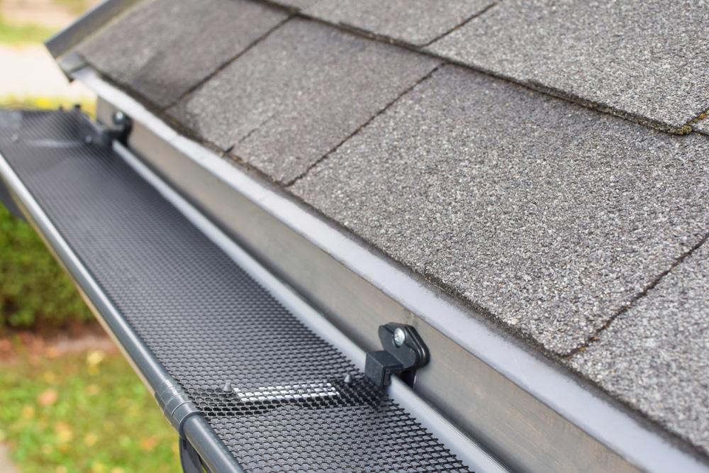 Plastic guard mesh over new dark gray plastic rain gutter on asphalt shingles roof at shallow depth of field