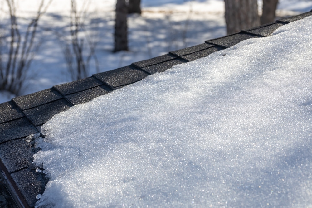 White snow begins to melt slightly on an asphalt shingle roof on a sunny winter day