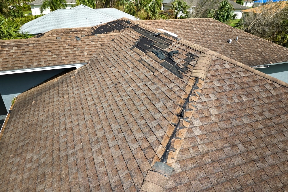 Damaged house roof with missing shingles after hurricane