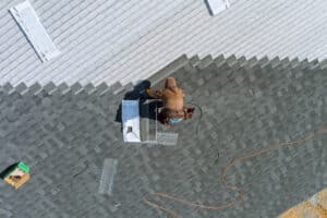 A worker uses an air hammer to nail new shingles for a roof