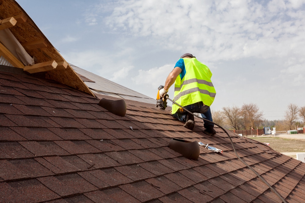 Construction worker laying asphalt shingles with a nail gun