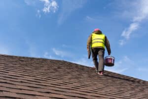 Unrecognizable and skilled workman in uniform standing on tile roof of new home with equipment