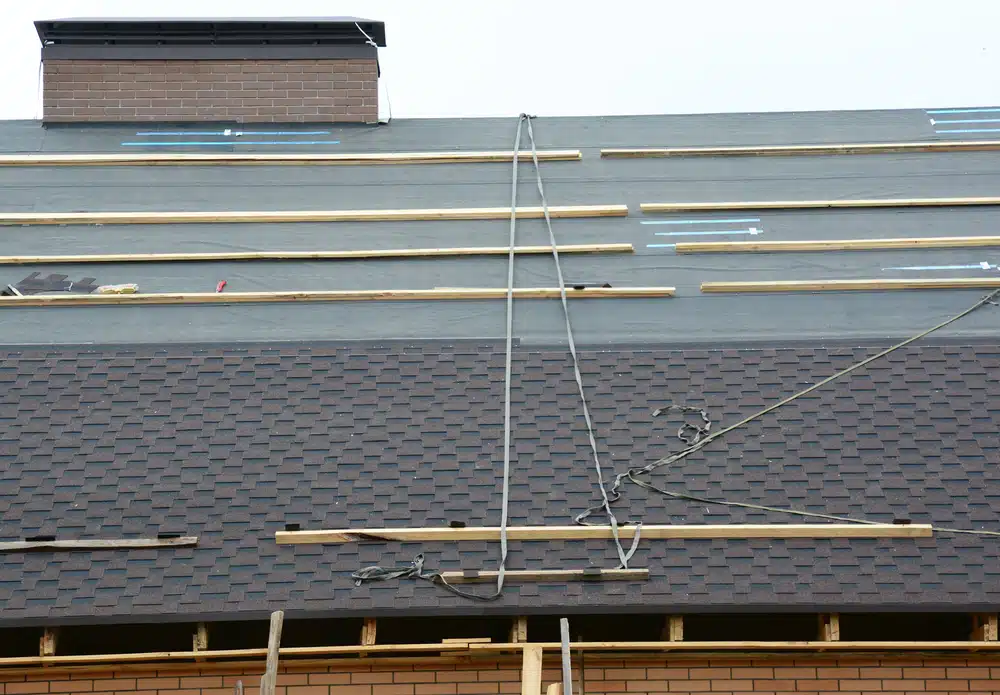 A close-up on a roof under construction with asphalt shingles installation on felt paper.
