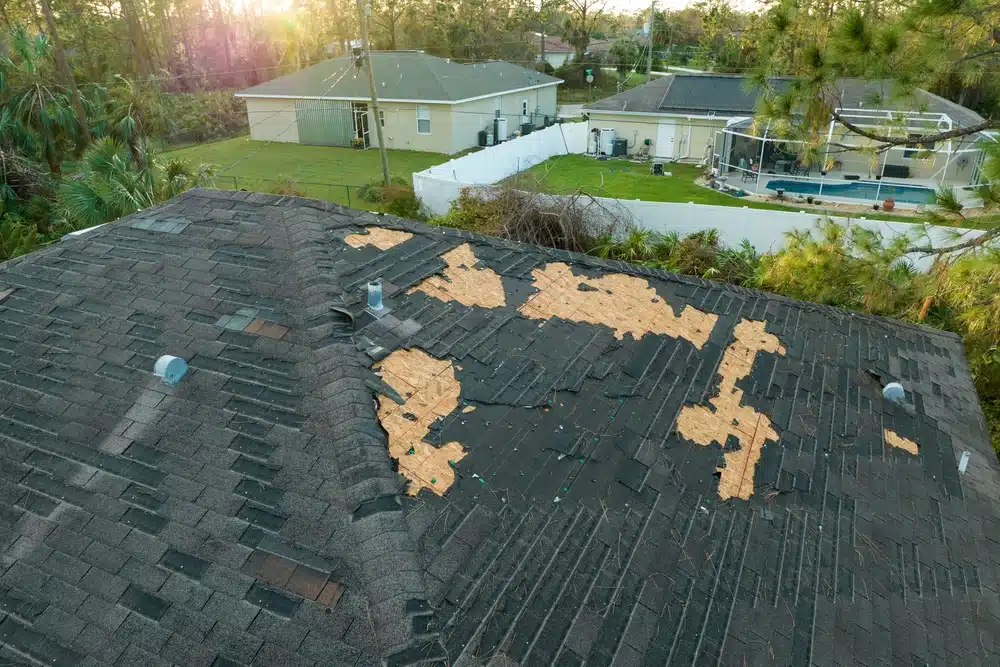 Ruined rooftop in need of repair. Wind damaged house roof with missing asphalt shingles
