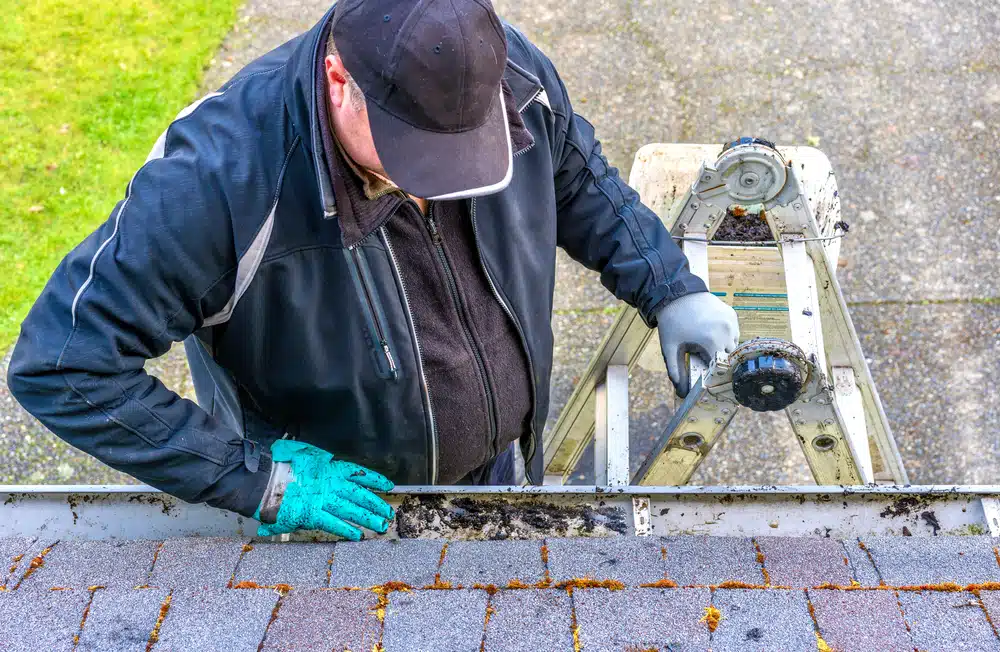 Man cleaning dirt from roof gutter on building
