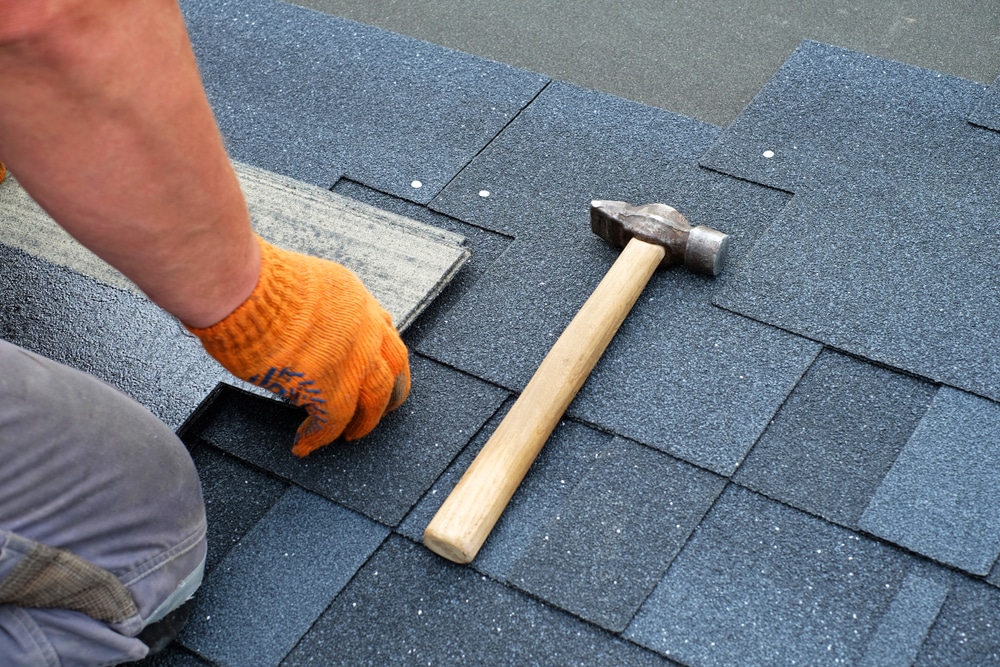 Contractor installing bitumen roof shingles with a hammer.
