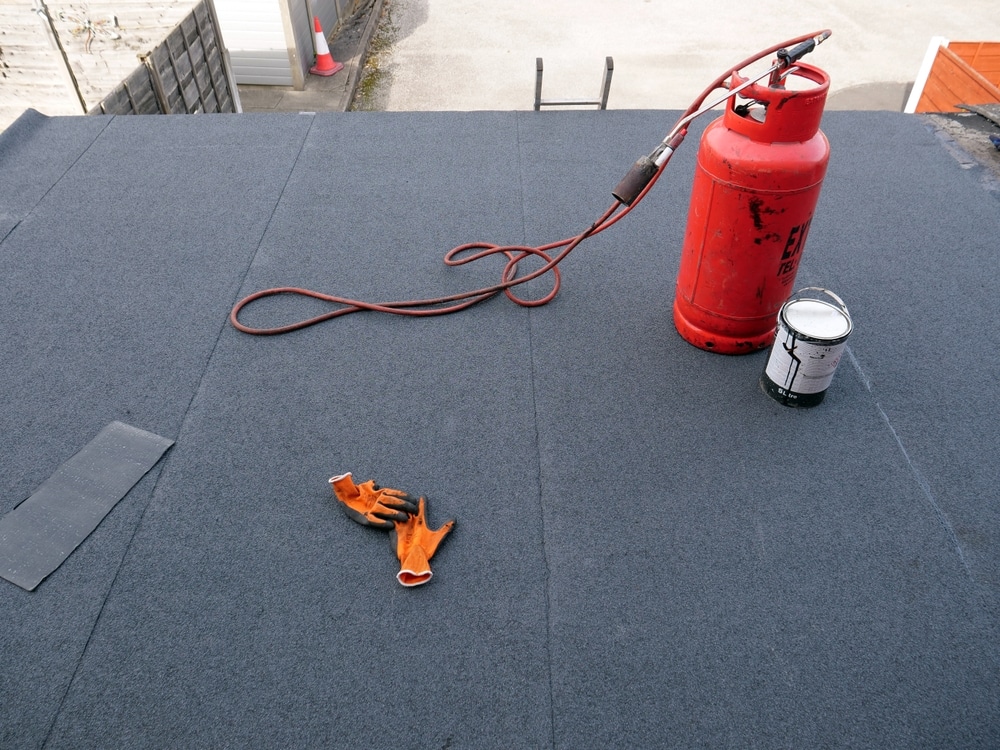 Red propane tank with blowtorch on bitumen-covered flat roof
