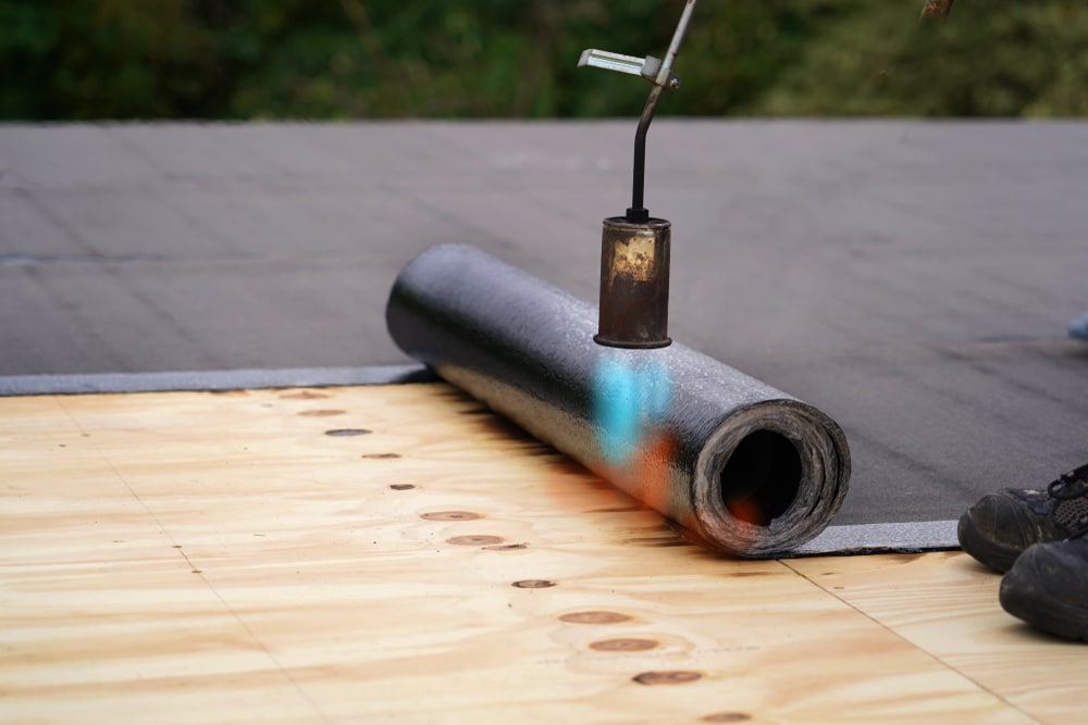 Flat roof installation with a gas burner and a roll of tar paper.