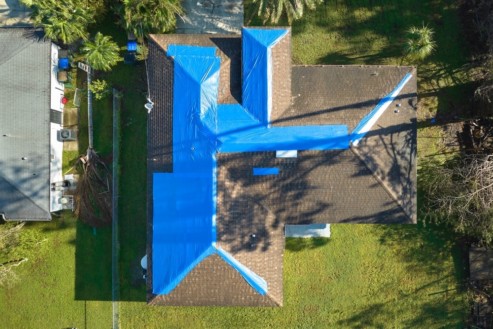 Aerial view of hurricane-damaged roof with blue tarp for protection.