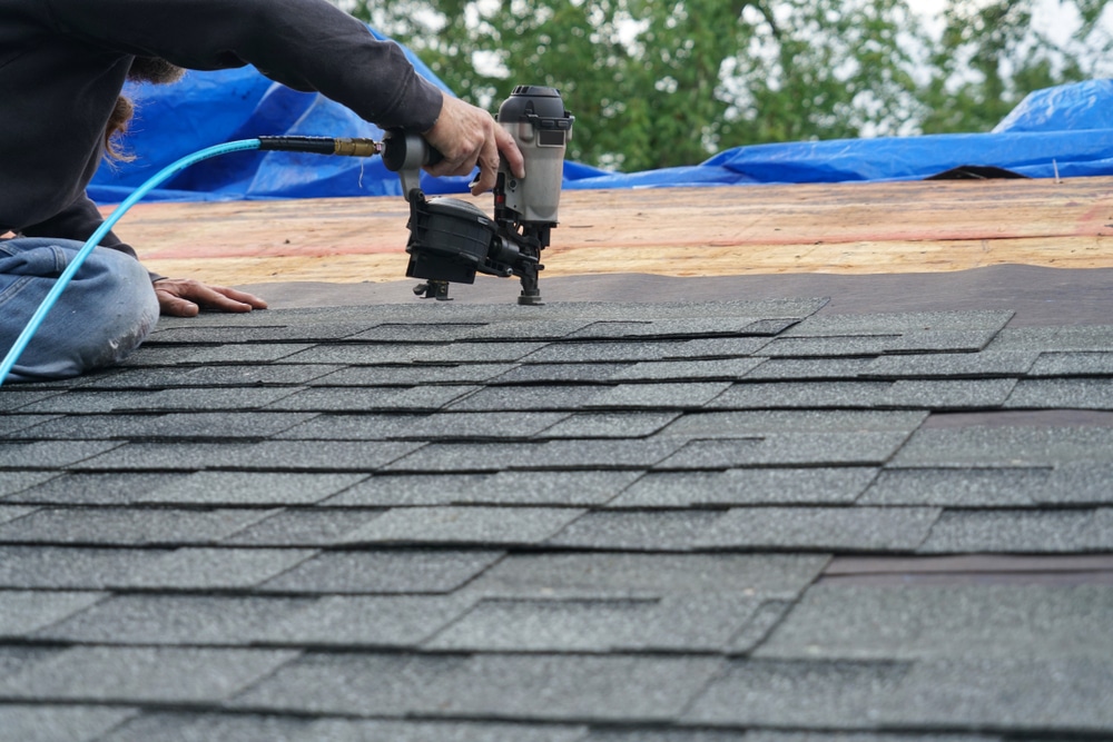 Handyman using nail gun to install shingle to repair roof