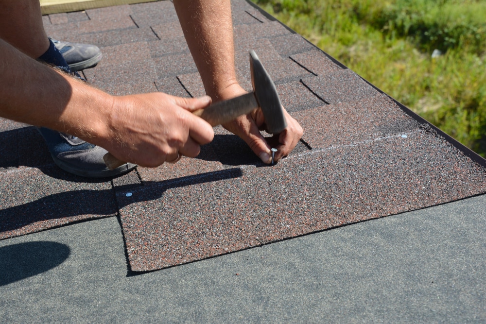 Roofer installing Asphalt Shingles on house construction roof corner
