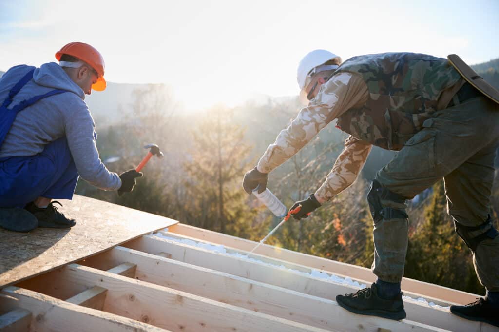 Male builder doing thermal insulation on roof of wooden frame house by polyurethane foam