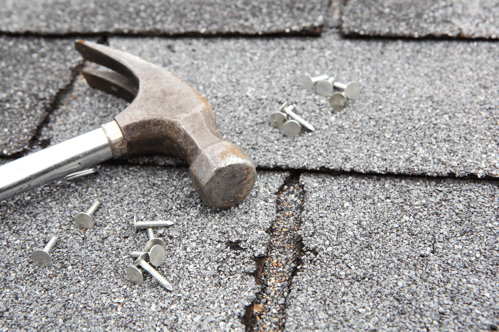 Hammer, roofing nails on grey-colored flat rooftop shingles, asphalt shingles, tools for roof repair
