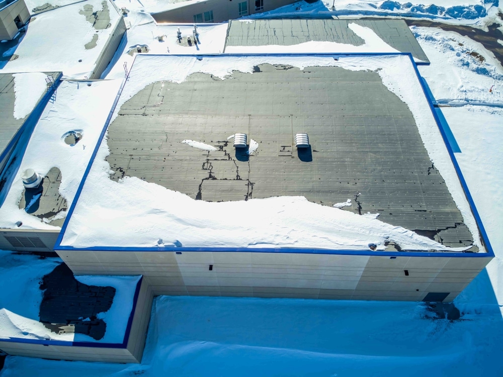 Elevated overhead drone view of a flat roofed building with snow load and ventilation units, on a land covered with snow