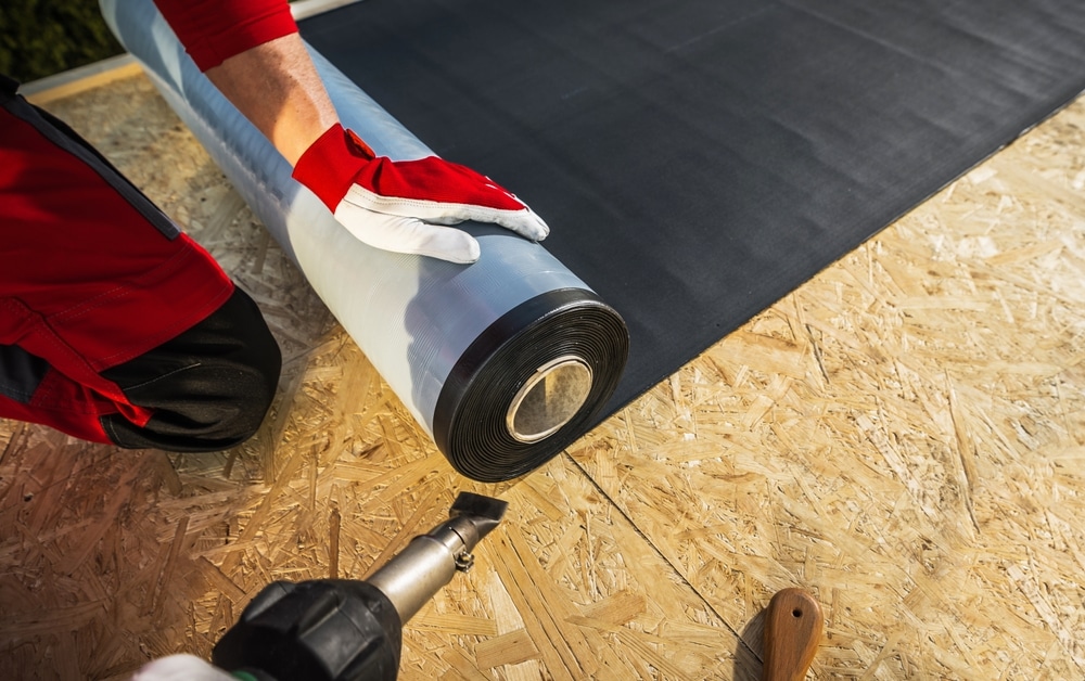 Roofer with roll of EPDM rubber membrane preparing to cover plywood roof