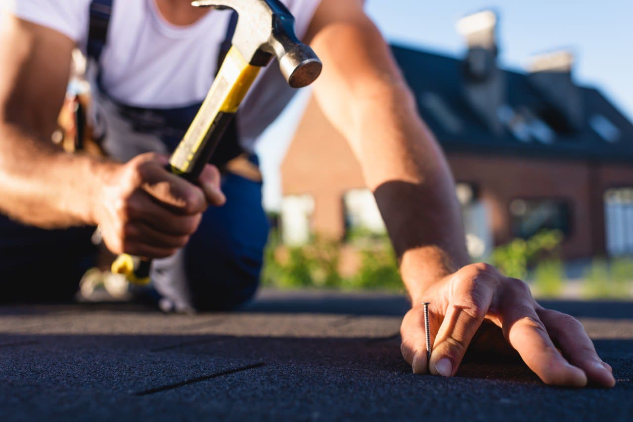 Cropped view of Roofing Expert Holding Hummer and Nail in his hands While Repairing Roof of a Building
