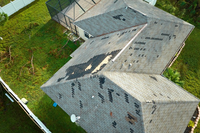 Top-view of a damaged house roof with multiple missing shingles after hurricane happened in residential area
