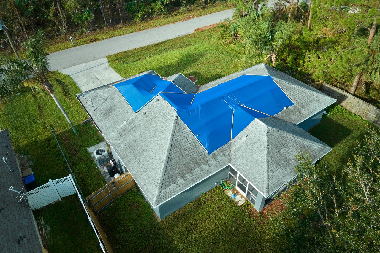 Hurricane happened, damaged house rooftop covered with protective plastic tarp against rain to prevent leaks