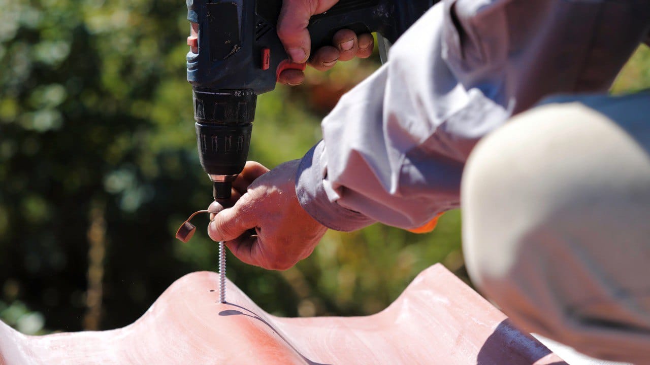 Male roof repair professional screwing a screw into the roof, working on installation of a roof of house
