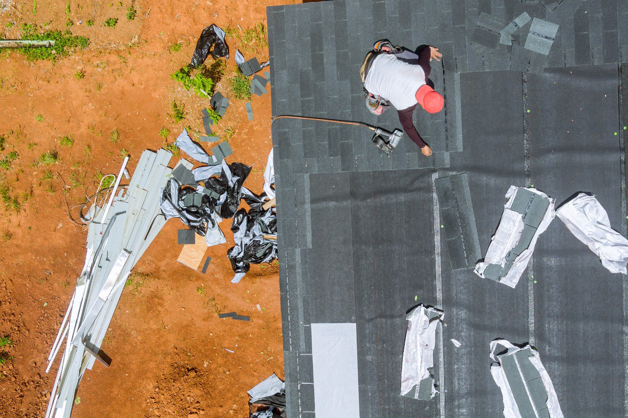 Top-view of an air nail gun is used by roofing contractor to install new asphalt bitumen shingles on roof of house
