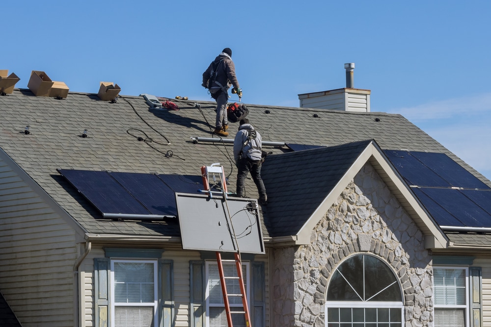 Technician workers installing alternative energy photovoltaic solar panels on house roof
