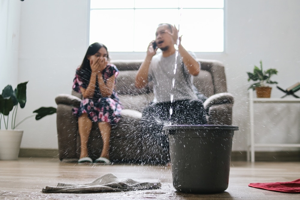 Woman and man sitting under a leaking roof, frustrated, willing to call to ask for professional help
