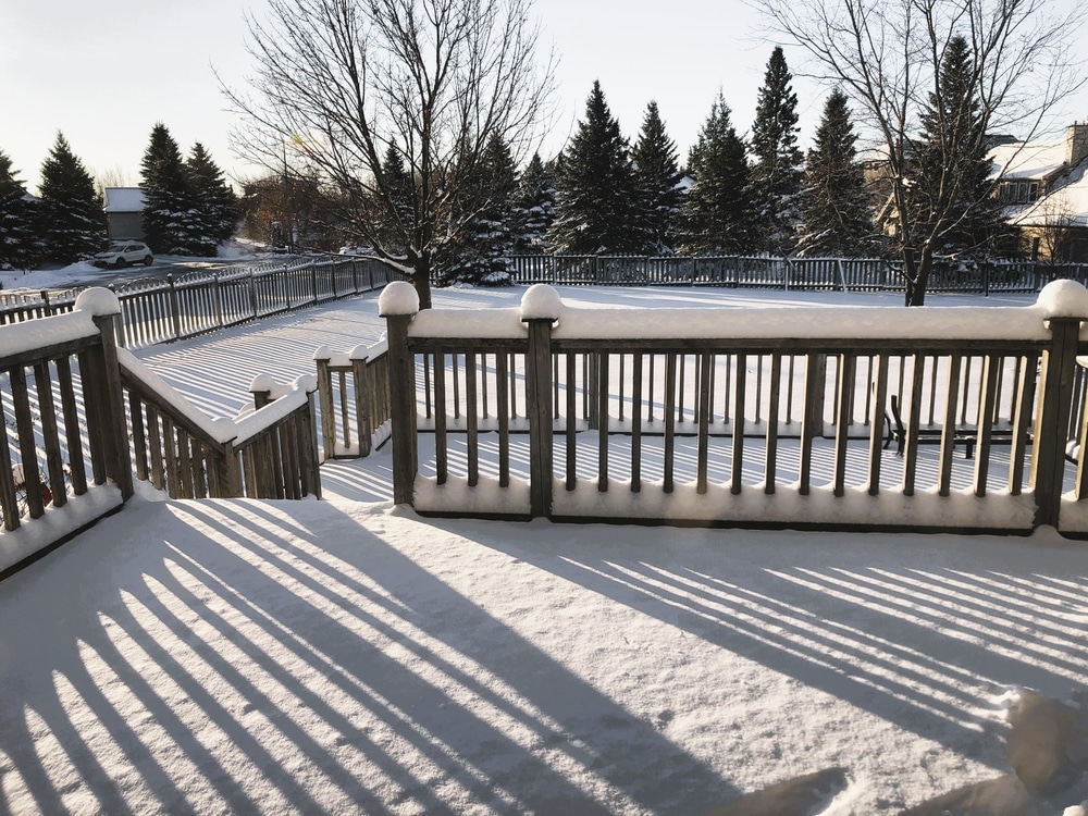 Late afternoon sun casts long shadows on the fresh white snow built up on the railings and posts of a backyard deck