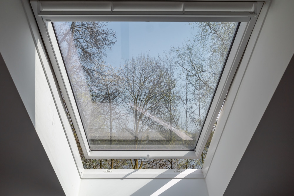 Close up view at slightly opening white Tilt Window Skylights at attic and defocused of outdoor tree in winter.