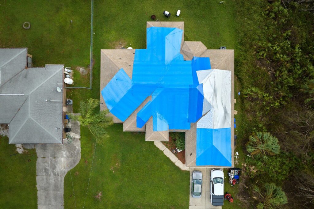 Damaged house rooftop, leaky roof covered with protective plastic tarp against rain water before roof repair