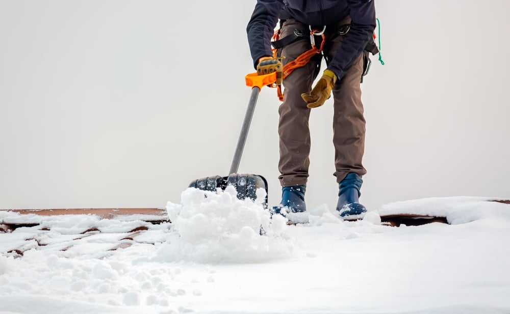 Professional roofing contractor - industrial climber removes snow from the building roof in winter, winter roof maintenance