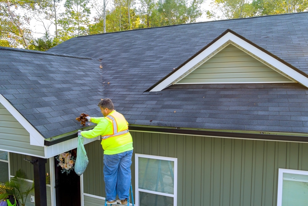 Roof gutter cleaning service contractor unclogging debris and fallen leaves to ensure smooth drainage and sound gutter
