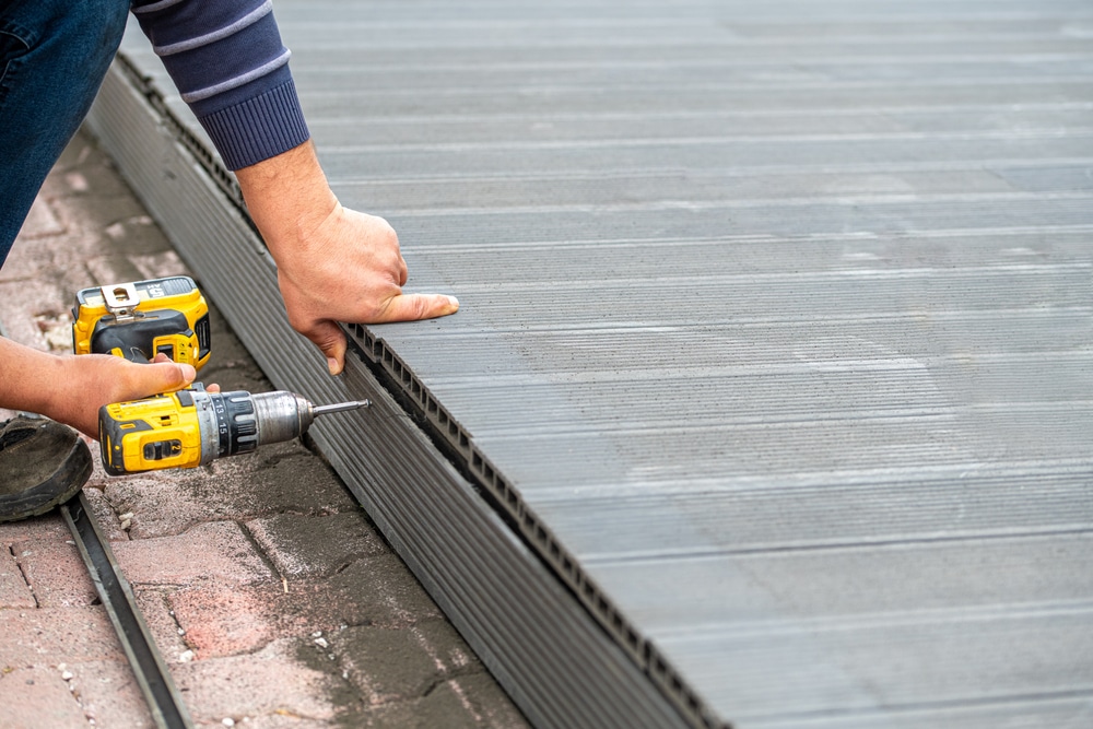 Male deck building contractor assembling composite deck using cordless screwdriver, gray-colored deck material
