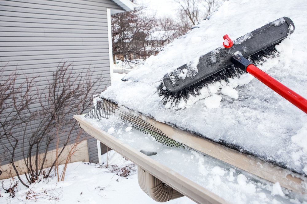 Close-up capture of removal of snow and ice from gutters a household broom for raking snow off of a roof