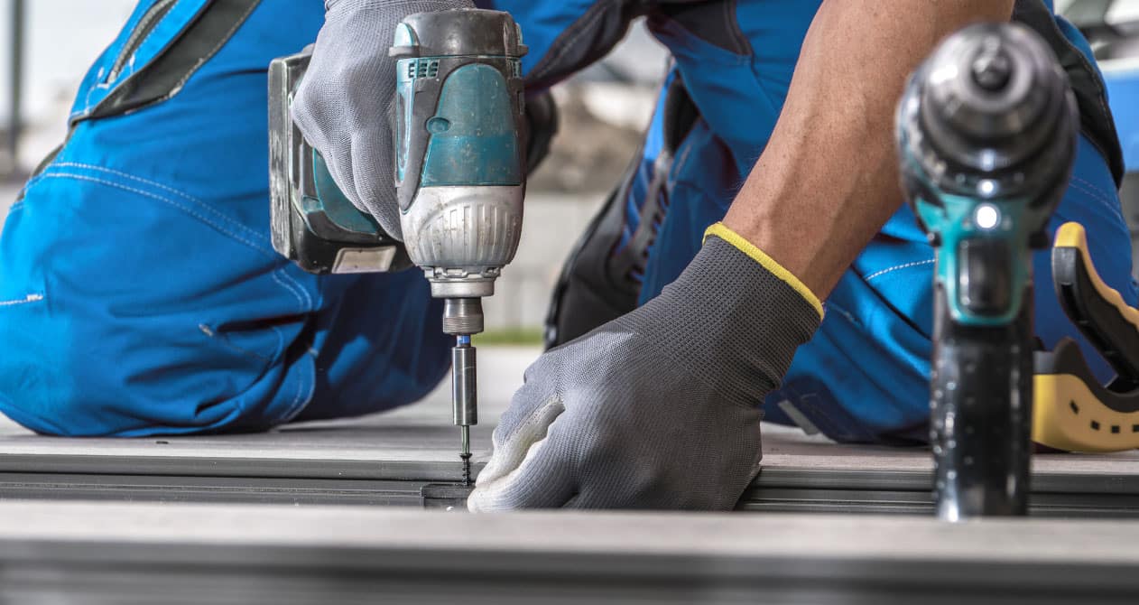 Close-up of a performing deck repair Boston, using a power drill to secure decking boards with precision and durable materials