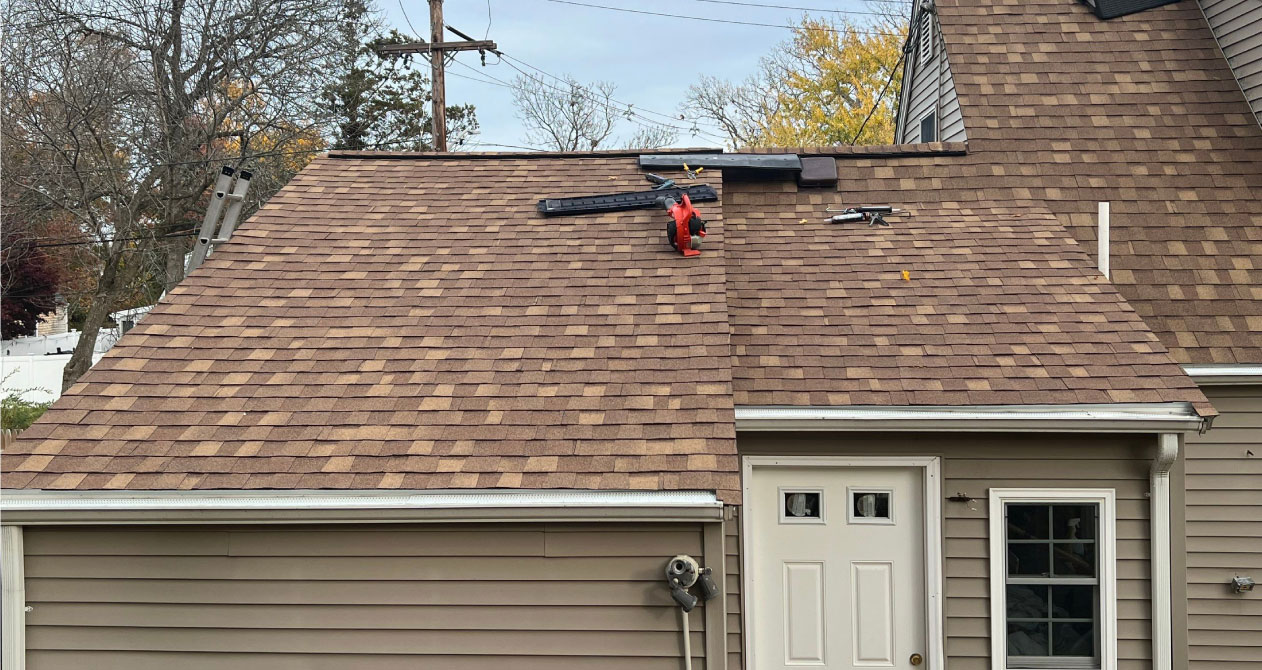 A partially repaired brown asphalt shingle roof with tools and equipment on top, indicating roof repair in Boston MA