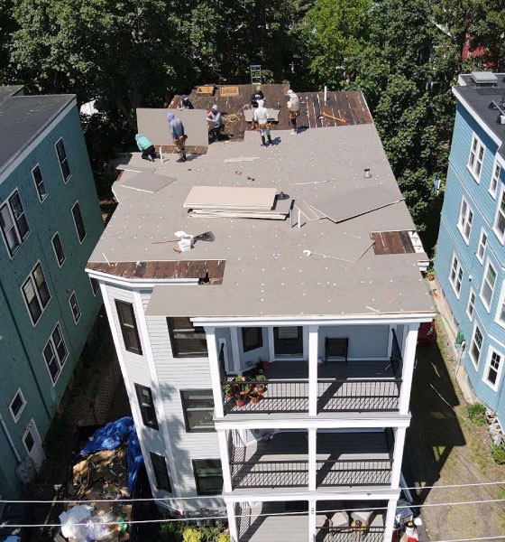 Workers installing a flat roofing system on a multi-story residential building, with panels and tools spread across the roof