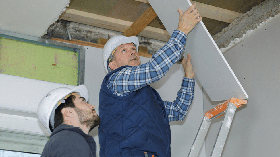 A builder installs drywall on a ceiling after fixing a roof leak, preventing further water damage and ensuring home protection