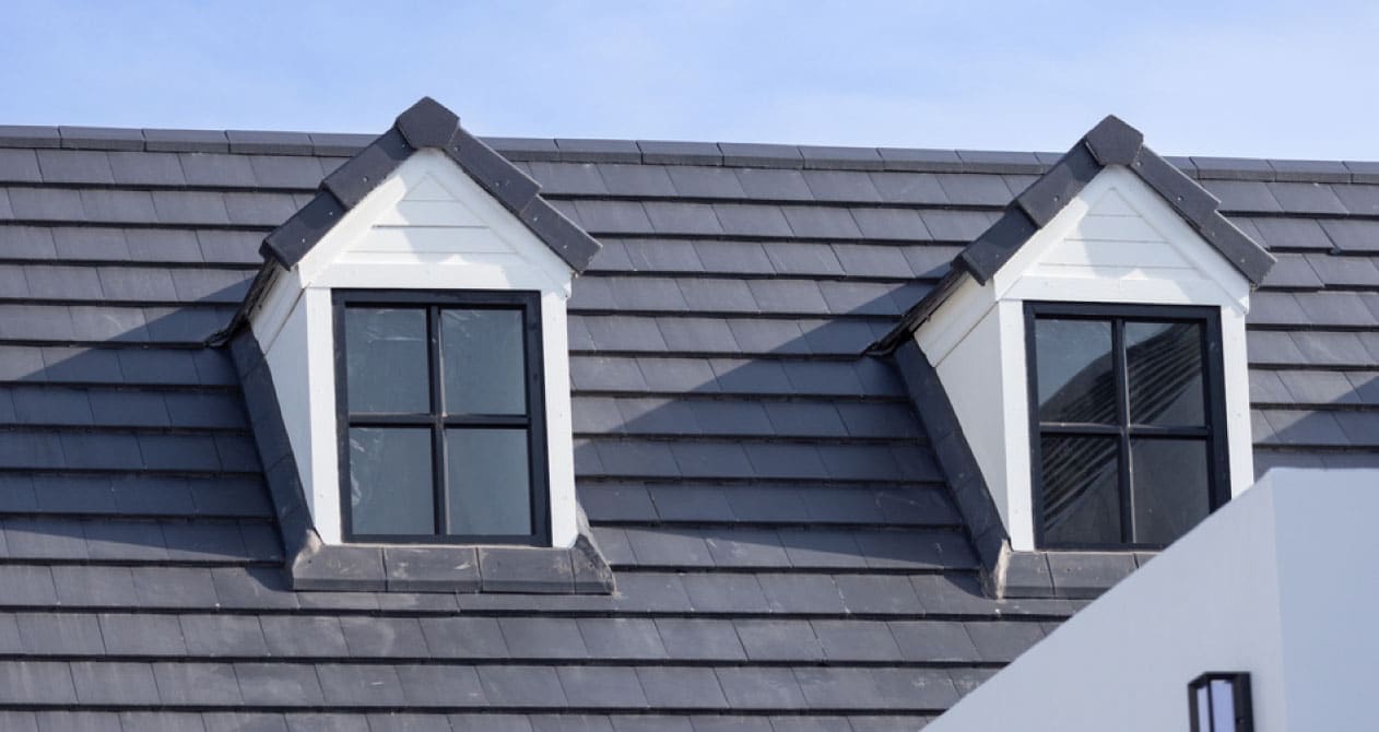 A dark gray slate roofing in Boston MA with two dormer windows featuring black frames and white trim, creating a modern look