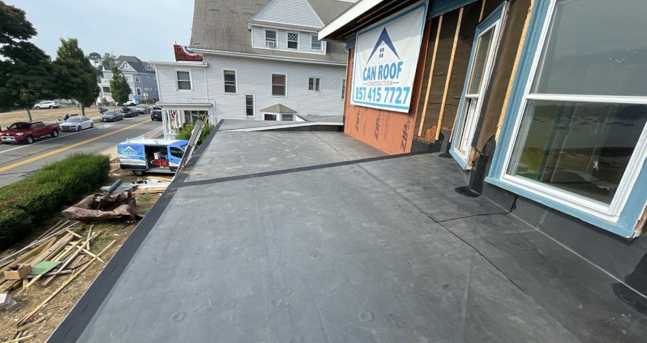 A newly installed black rubber roof on a building under construction, with a Can Roof sign, indicating rubber roofing in Boston