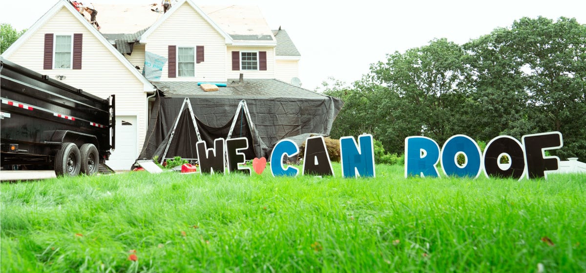 Roof replacement in progress on a residential home with "We Can Roof" sign in the yard. Trusted roofing company in Boston MA